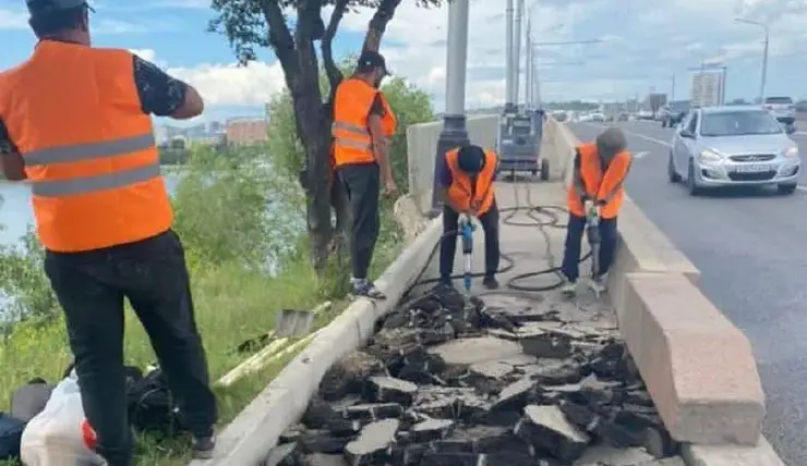 В Красноярске рабочие убирают старый асфальт с тротуара на Коммунальном мосту